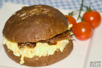 A brown wholemeal roll topped with sunflower seeds and filled with egg mayonnaise and streaky bacon